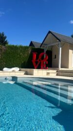 Sculpture LOVE rouge en métal au bord d’une piscine contemporaine