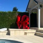 Sculpture LOVE rouge en métal au bord d’une piscine contemporaine