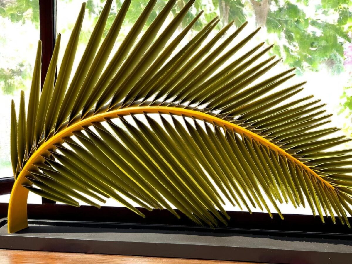 Sculpture de feuille de palmier en métal devant une baie vitré