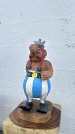 Gros plan sur le visage d’Obélix sculpté dans du bois, avec détails expressifs et finitions soignées
