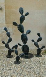 Sculptures en métal noir en forme de cactus disposées sur des graviers contre un mur en pierre