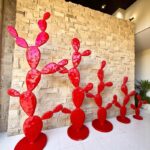 Sculptures rouges en métal en forme de cactus disposées devant un mur en pierre dans un intérieur moderne