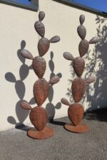 Sculptures en métal effet rouille en forme de cactus adossées à un mur beige en extérieur