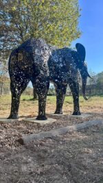 Statue d’éléphant noire en métal recyclé posée dans un espace naturel