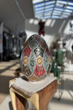 Grand œuf décoratif multicolore posé sur une table en bois dans une galerie d’art.