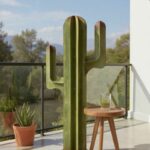 Sculpture verte en forme de cactus sur une terrasse ensoleillée avec table en bois.