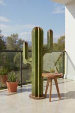 Sculpture verte en forme de cactus sur une terrasse ensoleillée avec table en bois.