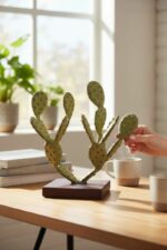 Petite sculpture en métal vert en forme de cactus posée sur un bureau lumineux