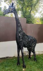 Sculpture de girafe en métal noir installée dans un jardin ou une cour extérieure