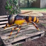 Statue monumentale d’abeille en métal peinte en jaune et brun, installation extérieure