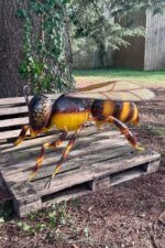 Statue monumentale d’abeille en métal peinte en jaune et brun, installation extérieure