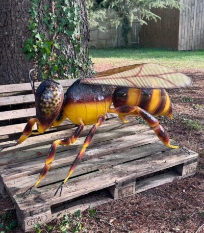 Statue monumentale d’abeille en métal peinte en jaune et brun, installation extérieure